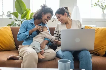 Two women with baby on couch with laptop